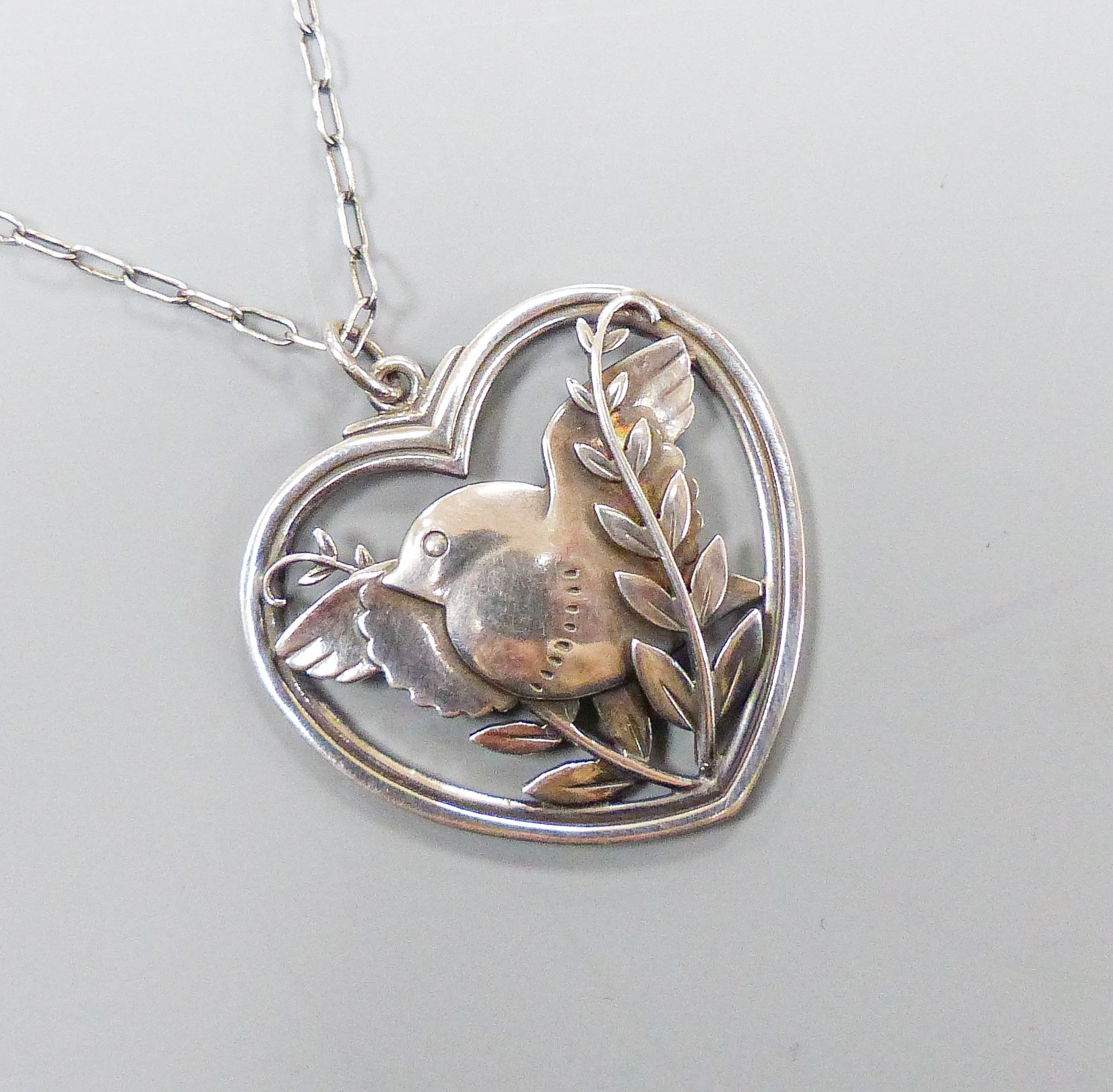 A Georg Jensen sterling 'Robin and frond' heart shaped pendant, no. 97, 38mm, on a white metal chain, 57cm.